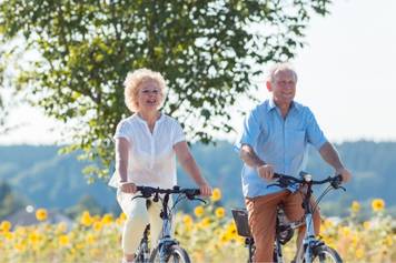 Hearing Aid Institute Billings Montana - An older couple riding bicycles through a field of sunflowers.