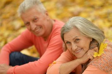 Hearing Aid Institute Billings Montana - An older couple sitting on the ground in autumn leaves.